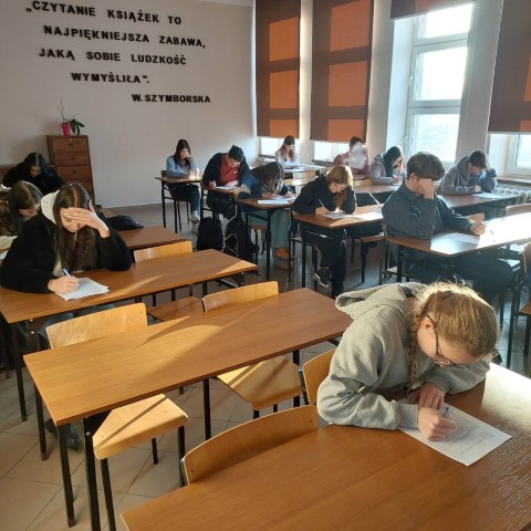 uczniowie siedzący w ławkach rozwiązują pisemne zadania konkursowe