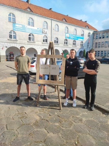 pieciu chłopców z drewnianą sztalugą z napisem książka ZSZ w tle budynek szkoły